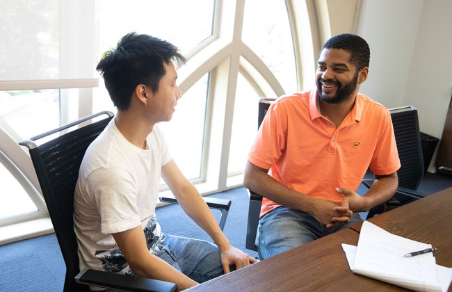 Annenberg faculty member MarlonTwyman speaks with a PhD student at a conference table