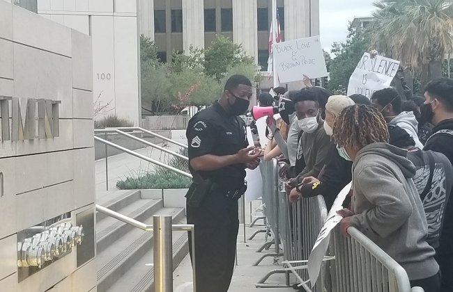 Photo of a Black police officer in front of a crowd of protesters