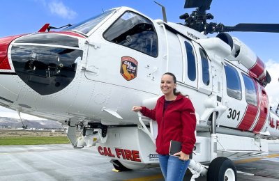 women in red hooded sweater poses in front of CAL FIRE helicopter
