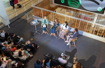 Spotify's Dustee Jenkins and Dean Willow Bay sit in the front of a crowd in the USC Annenberg Hall Forum on a stage with two student panelists. The shot if from above. 