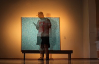Blurred person standing in front of an art piece on their phone.