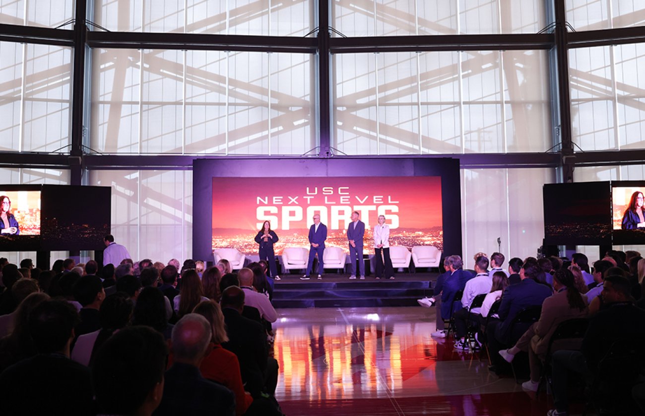 A stage that says "USC NEXT LEVEL SPORTS" on which four people are presenting.