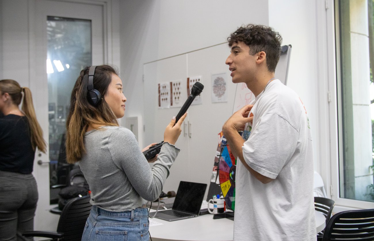 Asian female college student holds microphone and interviews male Hispanic college student