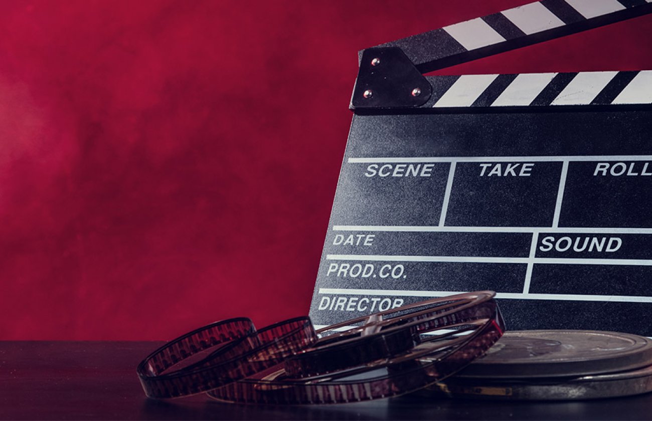 director's slate and movie film on table in front of gradient red background
