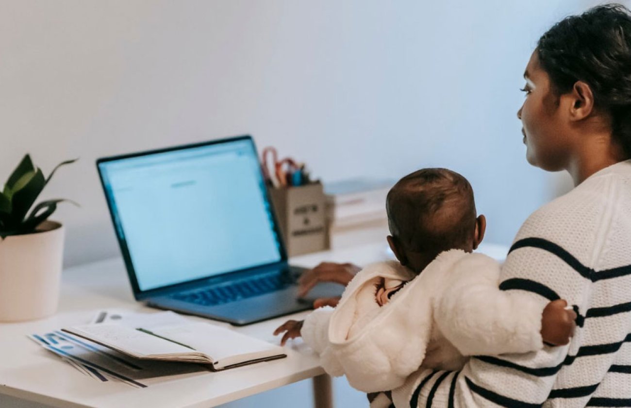 Photo of a person on a laptop holding a small child