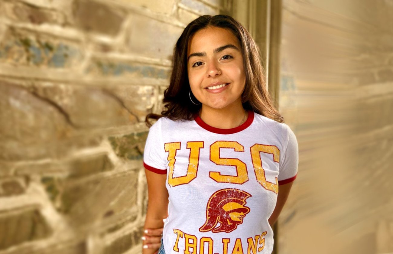 Incoming USC Annenberg master's student, Jenisty Colón, celebrates getting into USC by posing near a building with a USC t-shirt on.