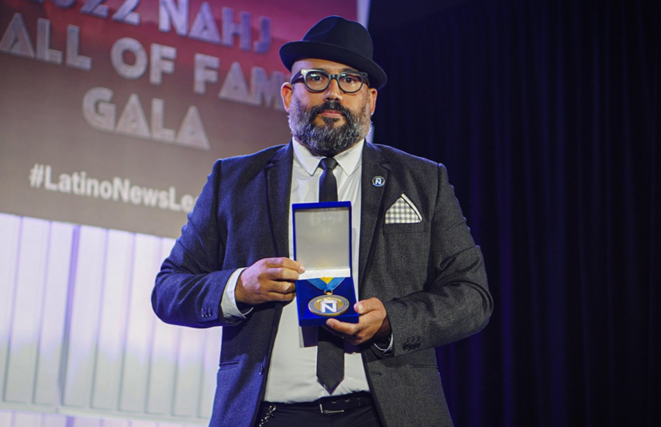 Professor Robert Hernandez holds his NAHJ award on stage.