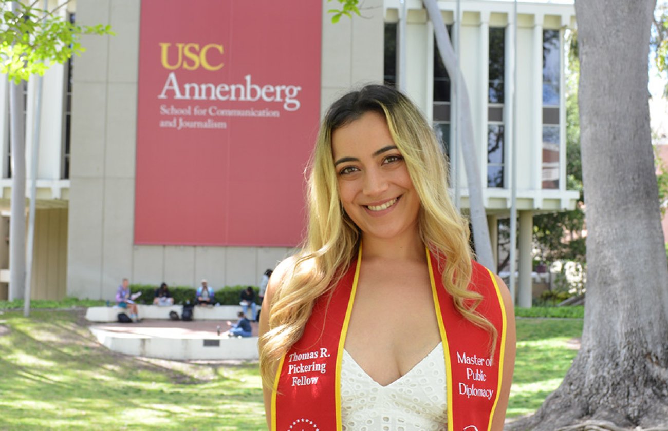 Hispanic women with red and gold graduation stole stands in front of USC Annenberg building