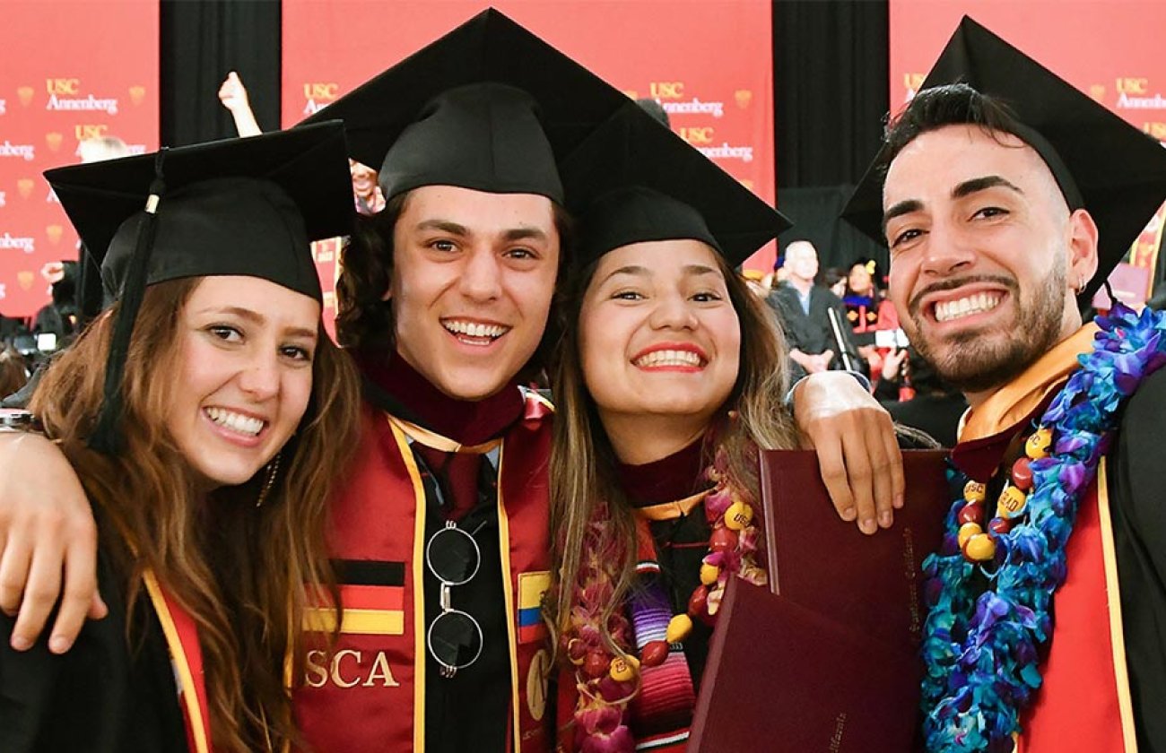 two male and two female students wearing graduation garb smile at the USC Annenberg 2023 commencement celebration.