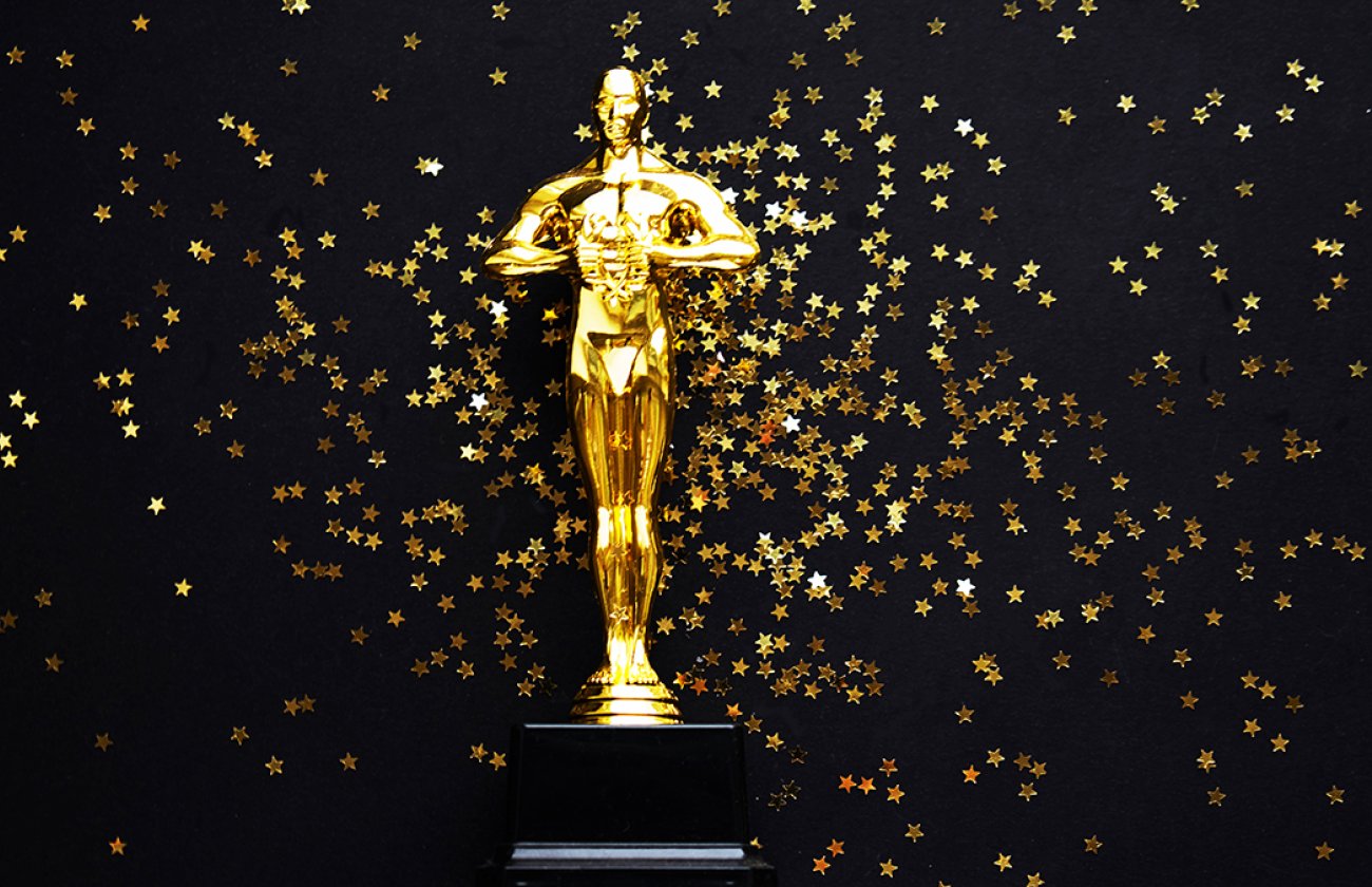 oscar award in front of black backdrop with gold confetti falling