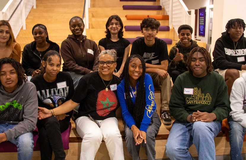 A group photo of Dr. Robin Stevens and a group of students smiling and sitting on the steps of Wallis Annenberg Hall. 