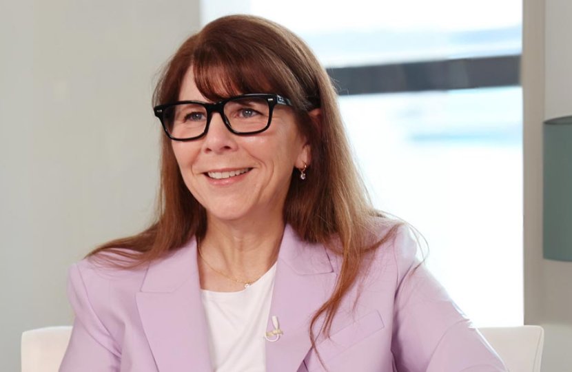 Stacy Smith smiling in front of a window wearing a light pink blazer. 