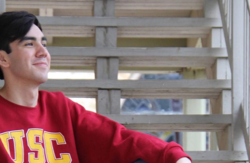 Young man sitting on white steps wearing a cardinal USC sweater.