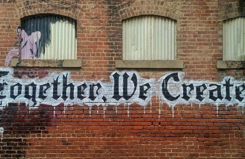 Brick wall with art that reads "Together We Create!"
