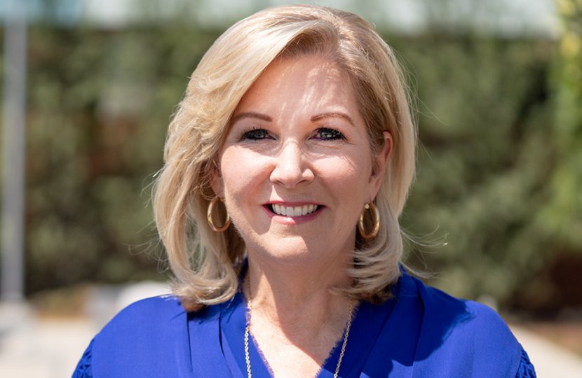 Women in blue shirt with shoulder length blonde hair posing outdoor and smiling for camera.