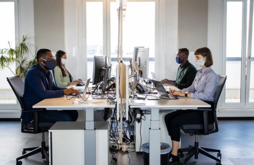 Photo of people sitting at a desk with face masks on
