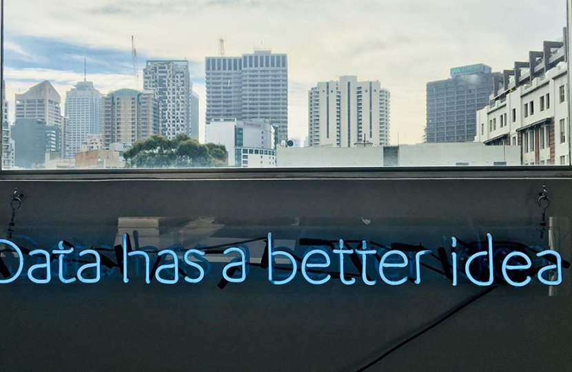 Photo of a blue neon sign under a city window that reads "data has a better idea"