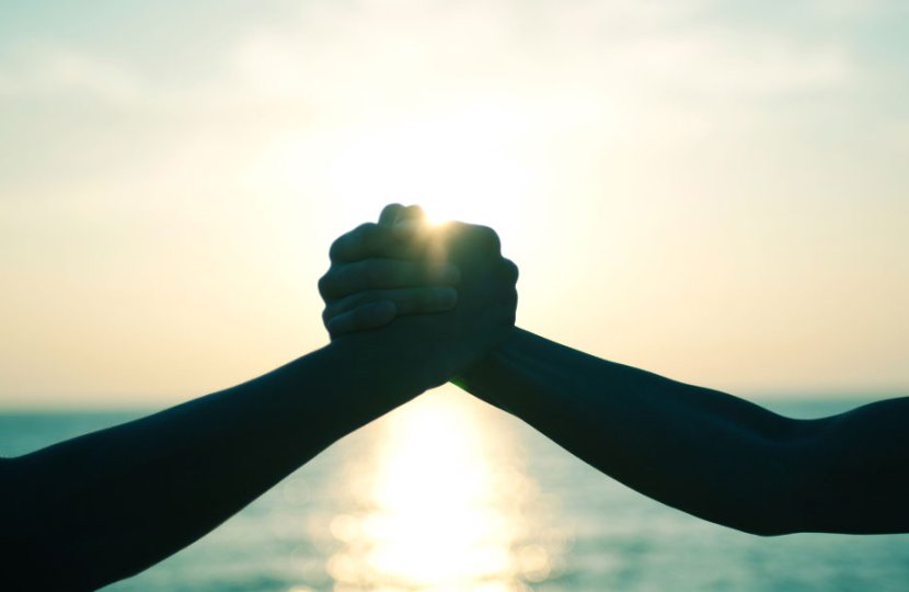 Photo of two hands together in front of a sunset