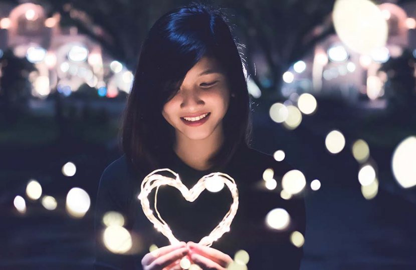Image of a person surrounded by lights holding a heart made of light
