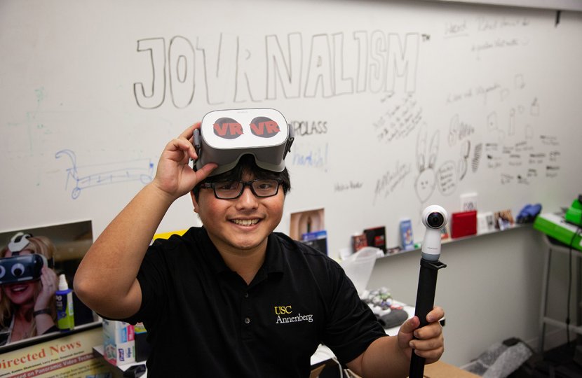 Photo of a person wearing glasses that say "VR" and with the word "Journalism" written behind them