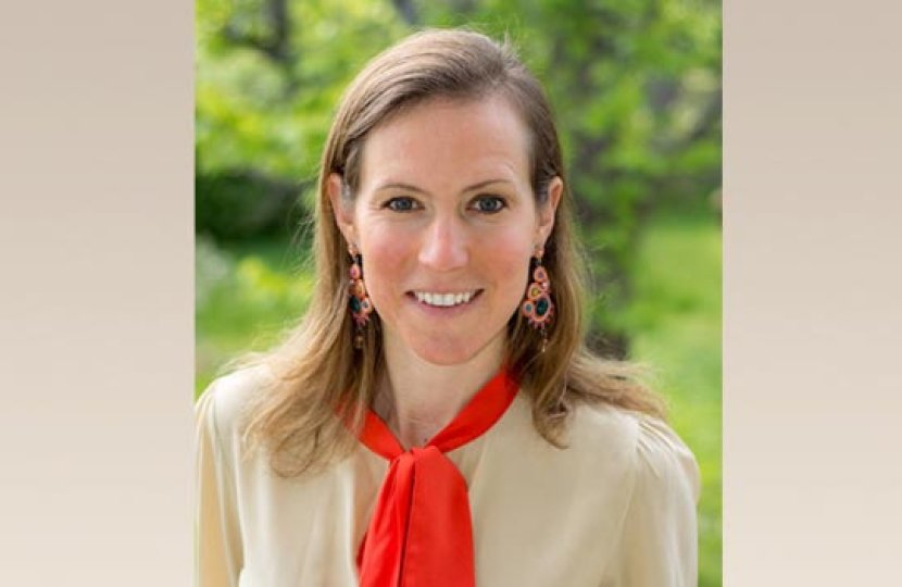 Headshot of Julie Banner, in which Julie Banner smiles at the camera with a green nature background and wearing a red scarf. 