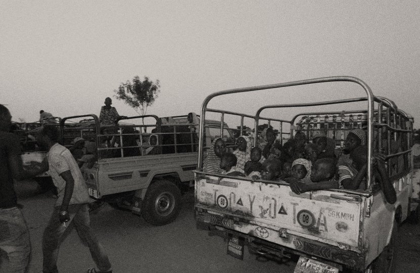 black and white photo of Nigerian women and children scared in back of truck as men walk around guarding