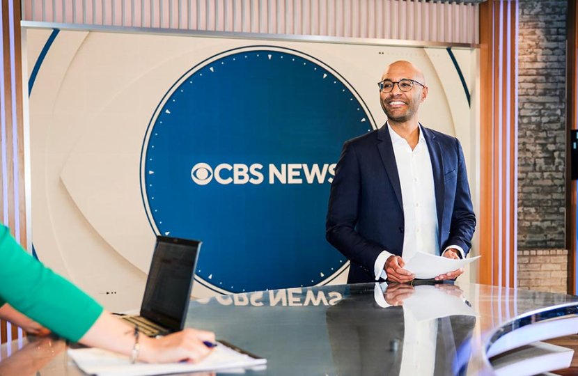 Anthony Galloway stands in front of CBS News sign while talking to female news anchor