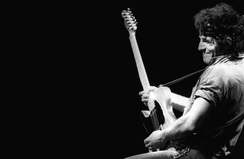 Bruce Springsteen playing guitar in black and white.