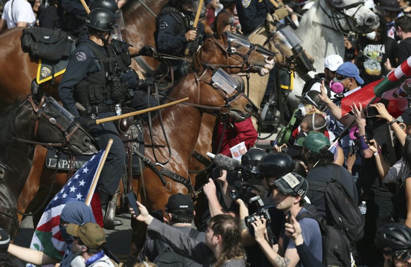 Police on horses with batons out stand amidst smartphone-wielding protesters. 