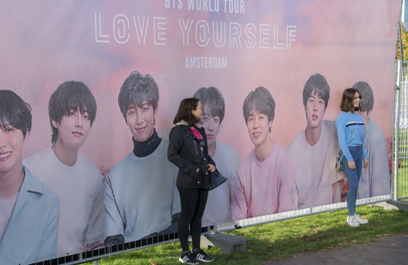 two girls pose in front of kpop idol poster