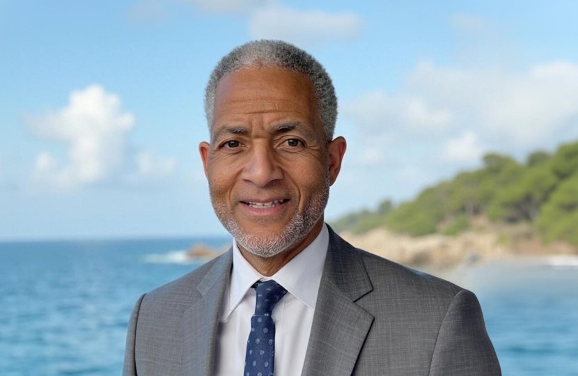 Andre Lapeyrolerie, from the shoulders up, smiling at the camera while wearing a suit and standing in front of an ocean with an island in the background. 
