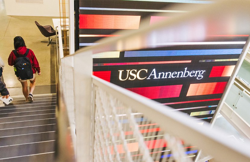 Students walking down a staircase while the Wallis Annenberg Hall Media Wall shines in the backgroud.