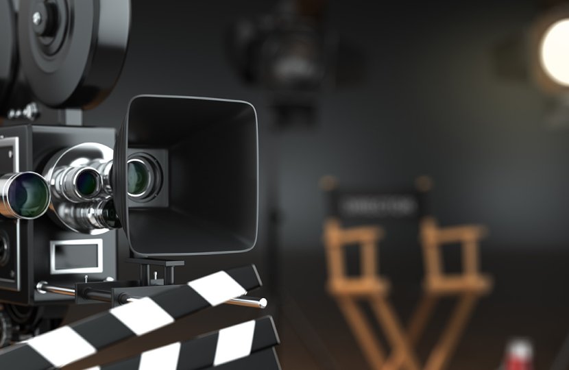 A film camera points off screen. A director's chair and a key light is in the background.