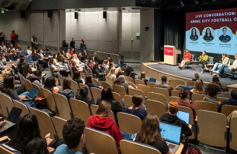 A full auditorium watches a panel of four women soccer players.