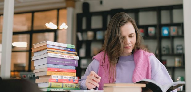 Photo of a person reading a book next to a stack of books
