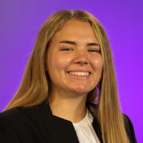 Headshot of a smiling young woman in front of a bright purple background. 