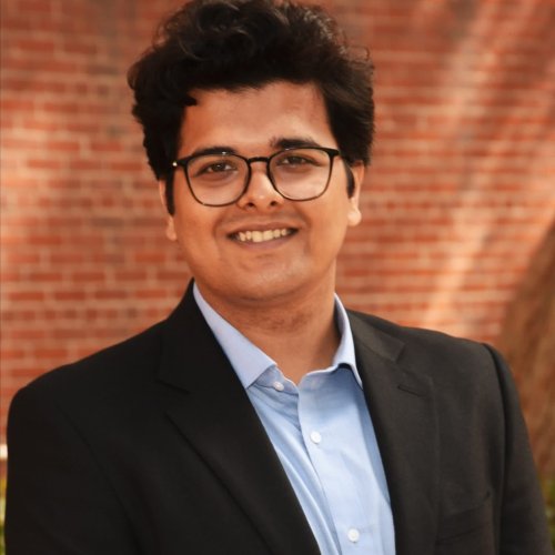 Headshot of a man smiling at the camera in front of a brick backdrop.