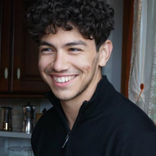 A young person in a kitchen and smiling at something in the distance.