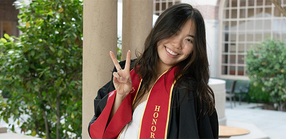 Joyce Gao holds victory sign and smiles in graduation robe
